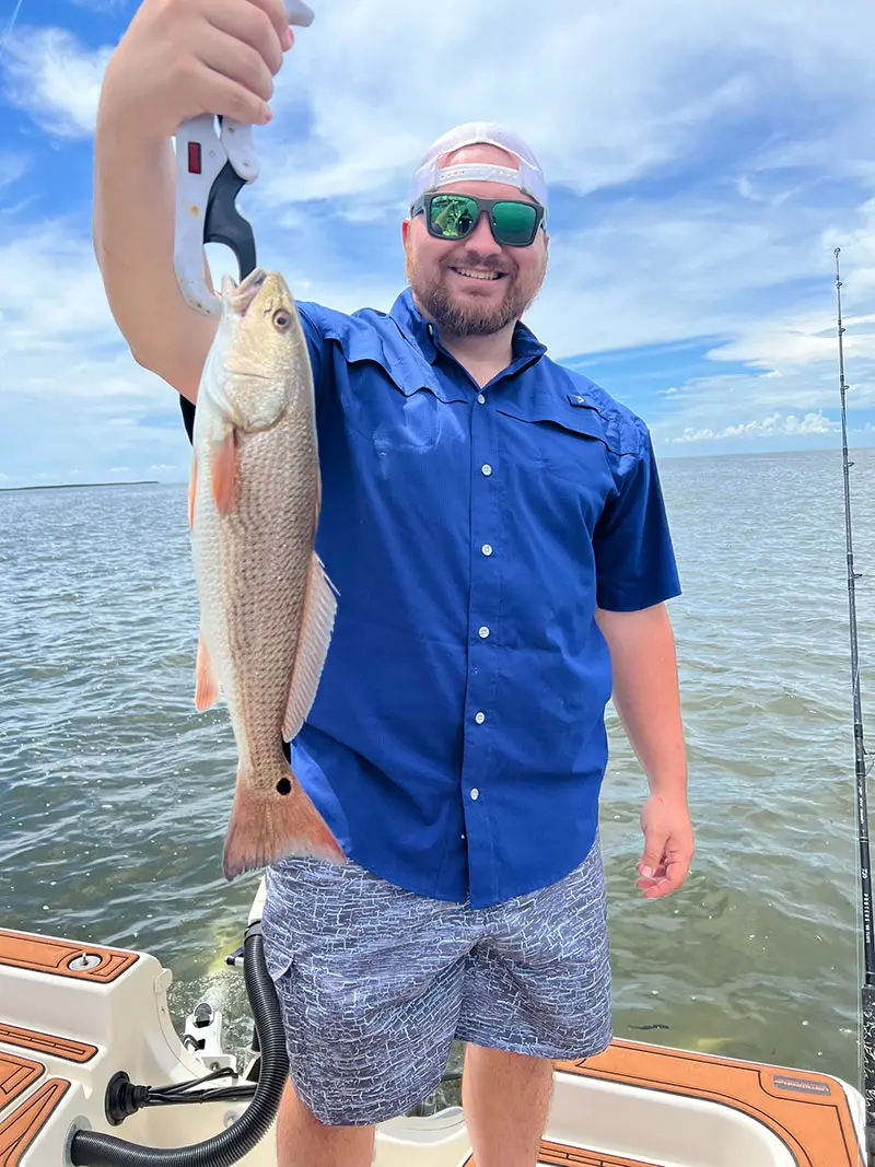 Smiling angler in a blue shirt holding a redfish on a lip grip aboard the boat on the inshore flats