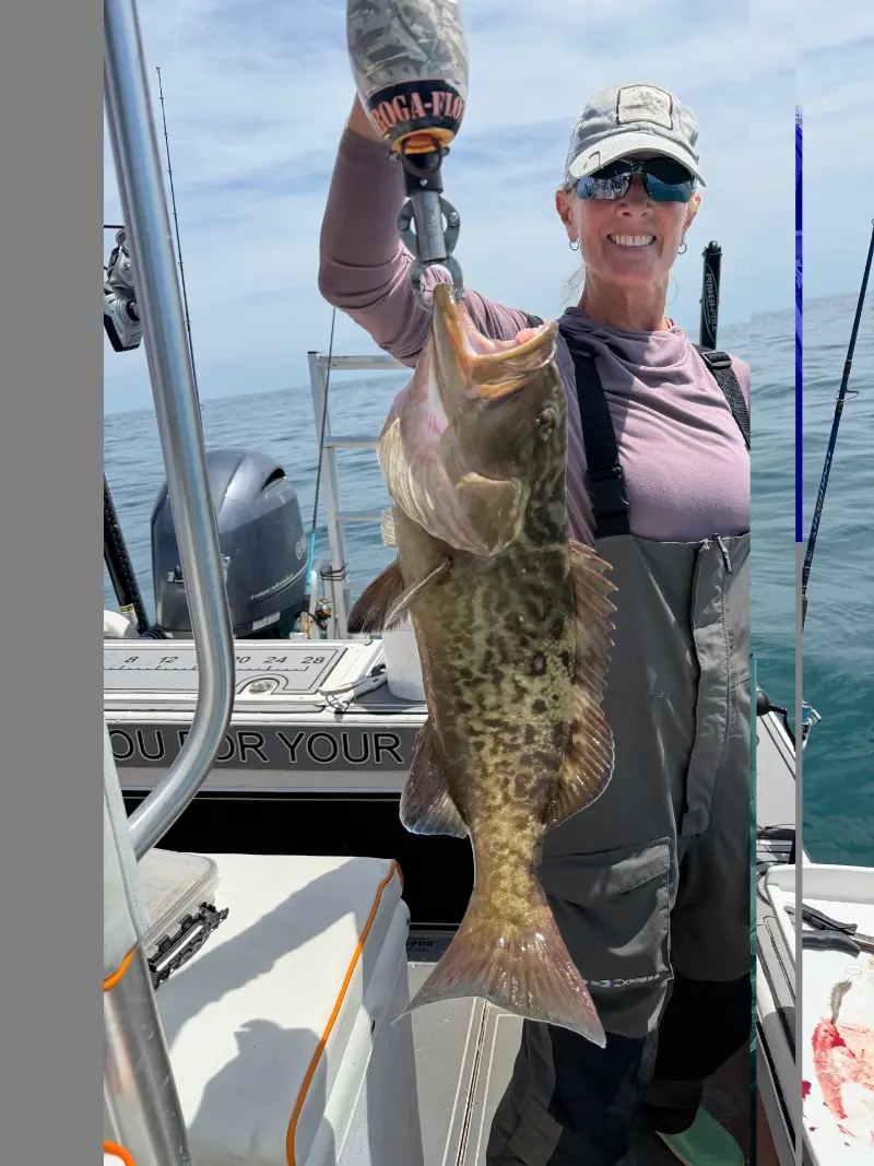 Woman in bibs holding up a gag grouper on a Boga grip at the stern of a boat