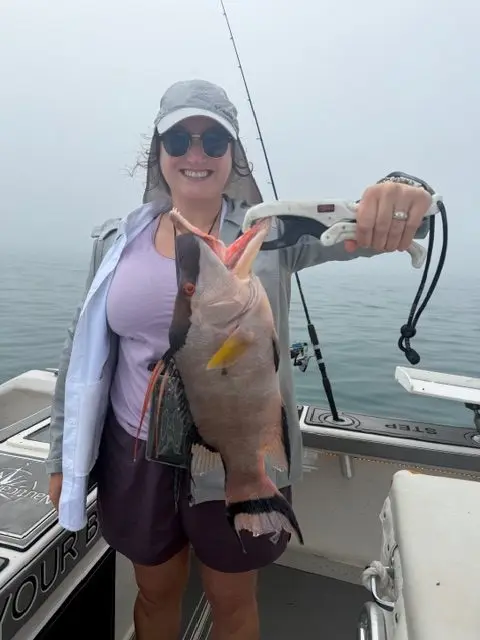 Woman holding a hogfish on a fish grip on a foggy morning aboard a boat