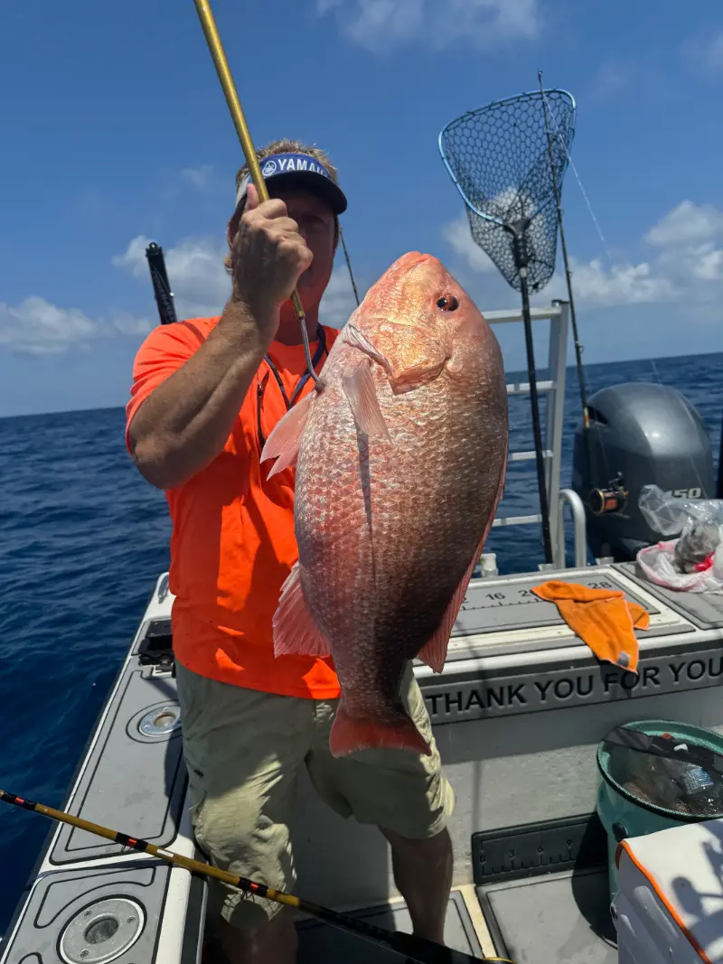 Angler in an orange shirt holding a red snapper by the leader beside a Yamaha 150 outboard