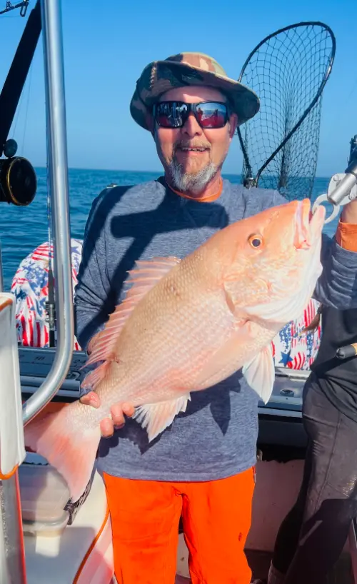 An angler in a camo hat holds a large red snapper with both hands aboard a boat