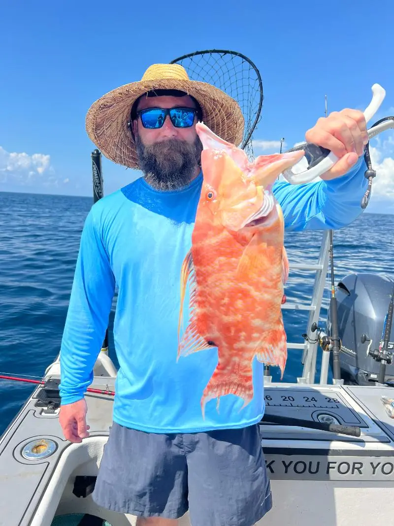 Bearded angler in a straw hat holding up a large hogfish on a Native Charters boat