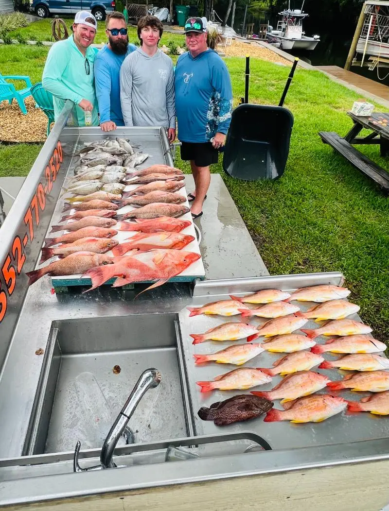 Four anglers at the Native Charters cleaning table with red snapper, lane snapper and mangrove snapper laid out