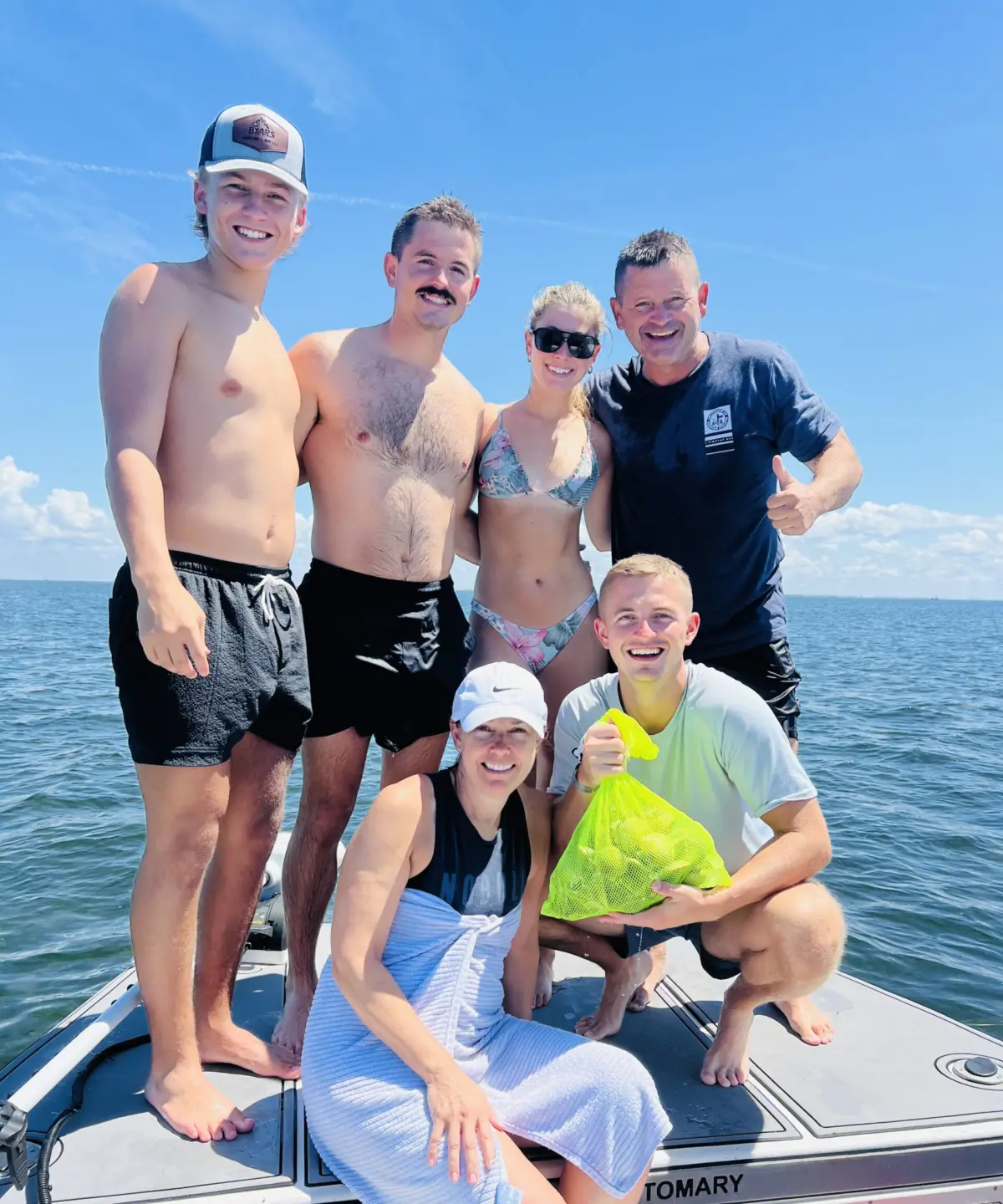 Family of six on the bow of a Native Charters boat with a mesh bag of bay scallops