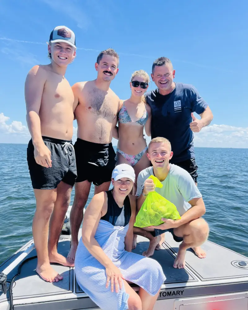 Family of six on the bow of a Native Charters boat with a mesh bag of bay scallops