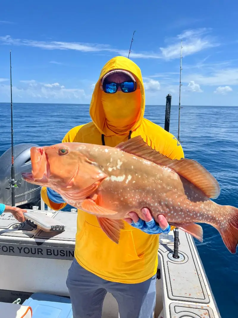 Angler in a yellow hoodie holding a red grouper broadside on a Native Charters boat