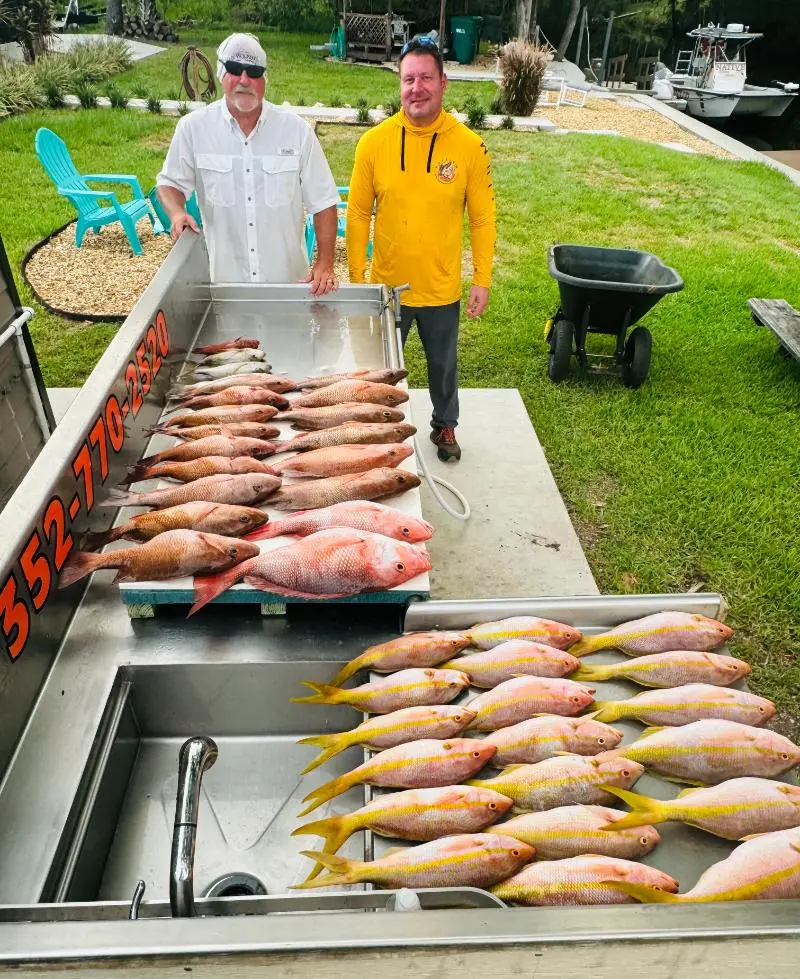 Two anglers at the Native Charters cleaning table with yellowtail snapper, red snapper and mangrove snapper