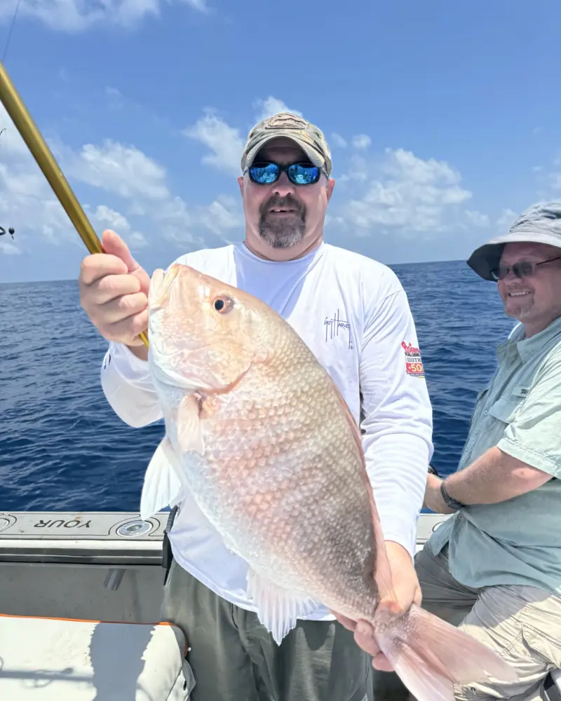 Angler holding a large red snapper across his chest with a second angler smiling beside him