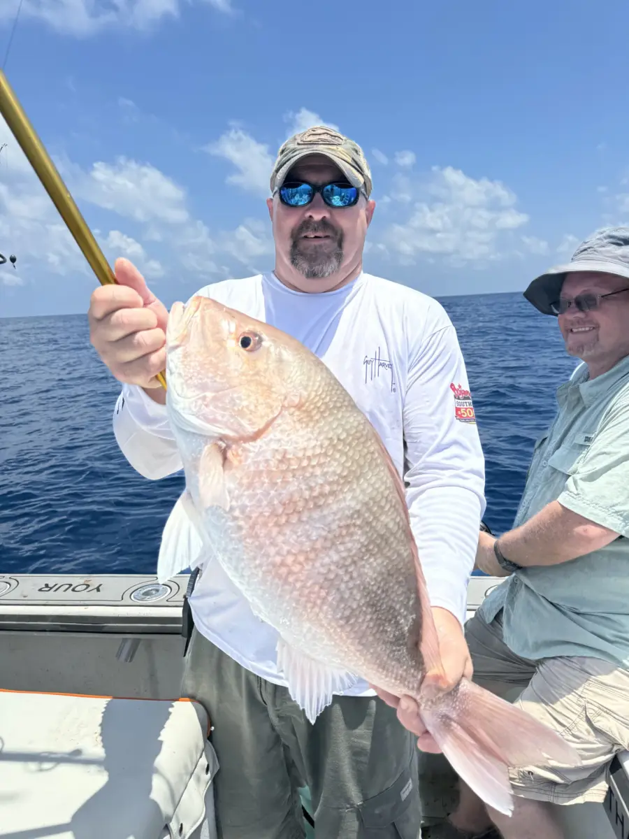 Angler holding a large red snapper across his chest with a second angler smiling beside him