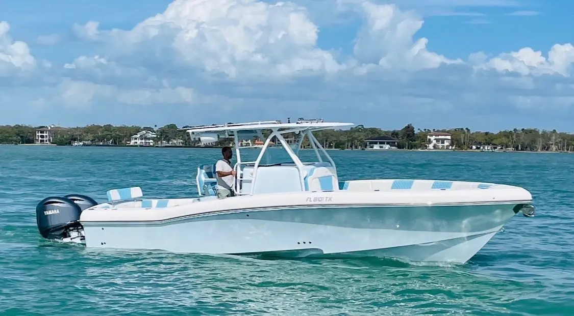 Man at the helm of a white center console boat with twin Yamaha outboards on calm water