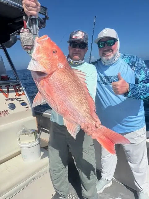 Two men on a boat, one holding a large red snapper on a Boga grip and the other giving a thumbs up