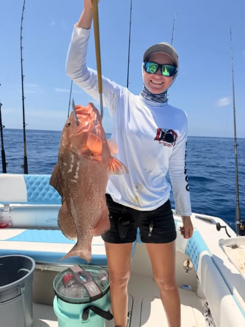 Woman angler holding up a red grouper on a lip gripper aboard the Native Charters center console