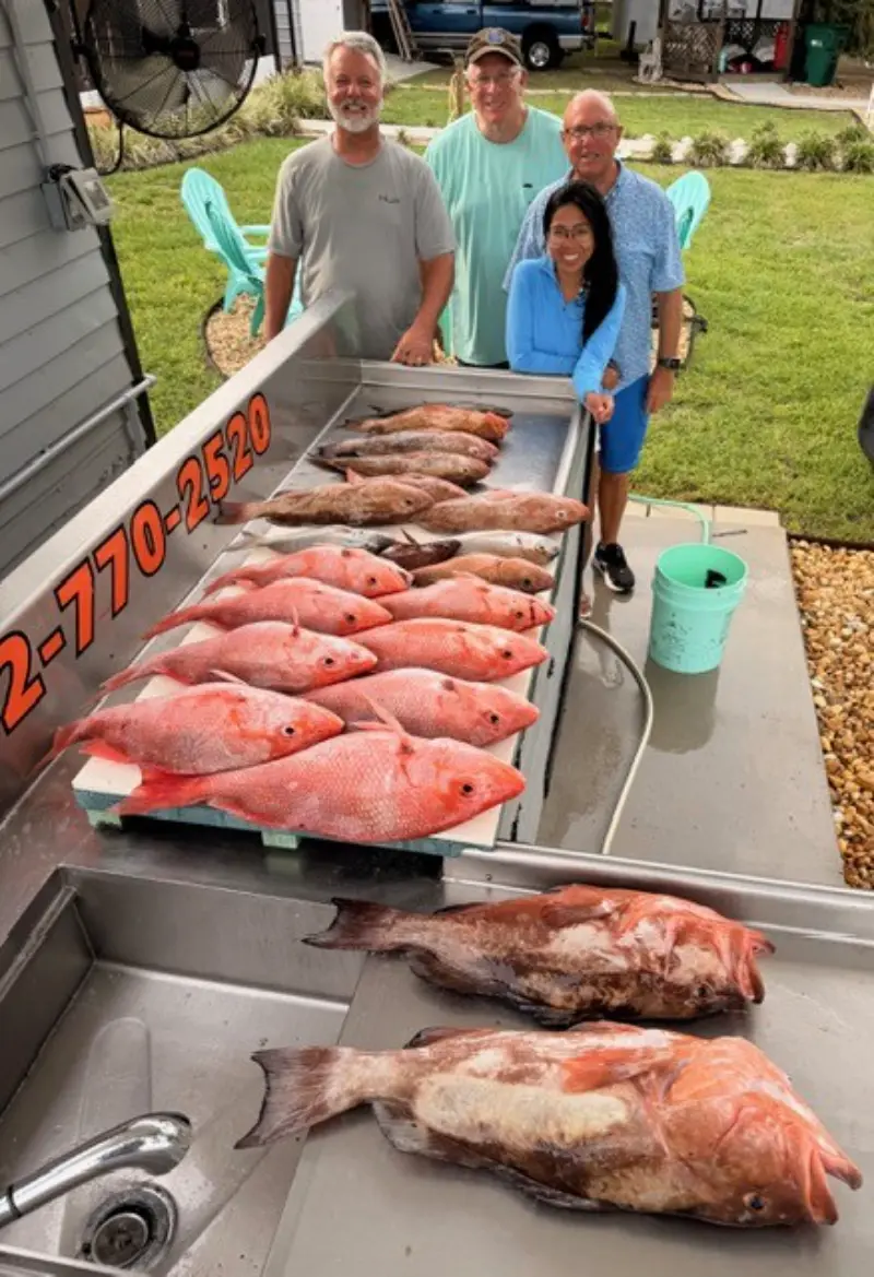 A day's catch of red snapper and grouper laid out on the Native Charters cleaning table with four anglers standing behind