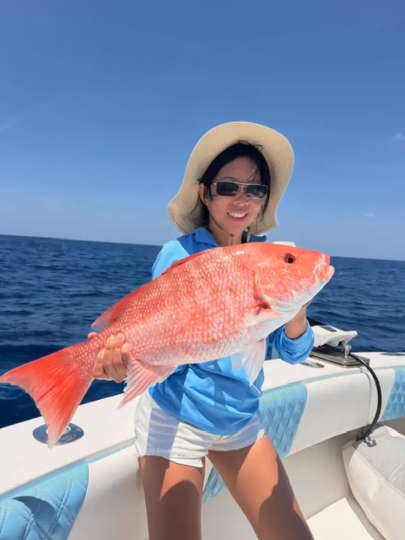 Smiling woman in a sun hat holding a red snapper aboard the Native Charters center console offshore