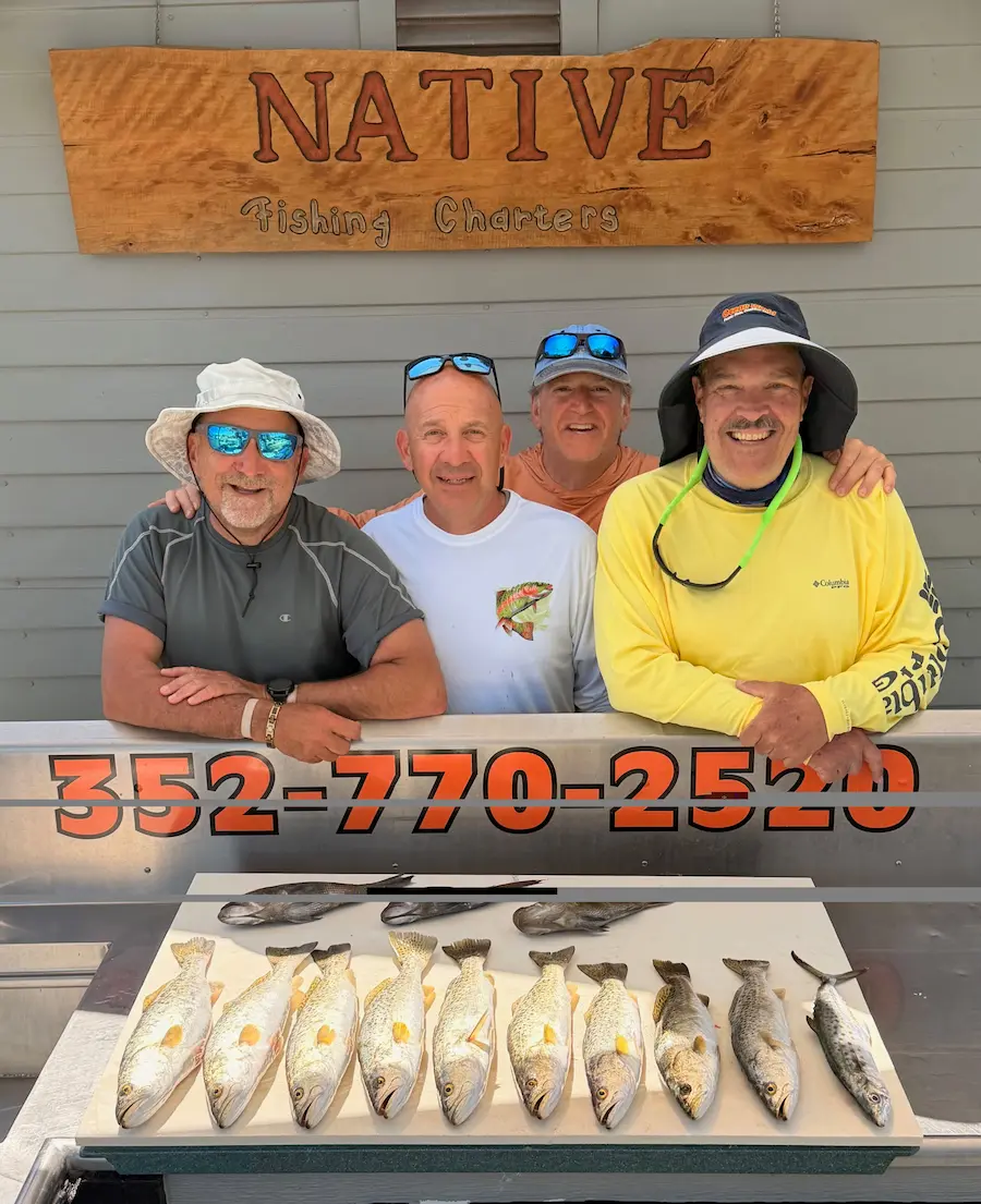 Four anglers under the NATIVE Fishing Charters sign with a row of spotted seatrout on the cleaning table