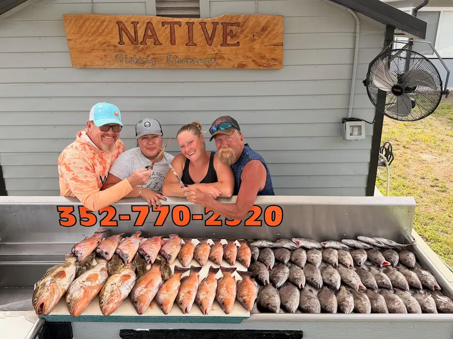 Four anglers at the Native Charters cleaning station with a table of hogfish, grouper and mangrove snapper