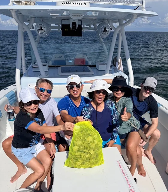 Six adults on a Native Charters boat holding a mesh bag full of bay scallops